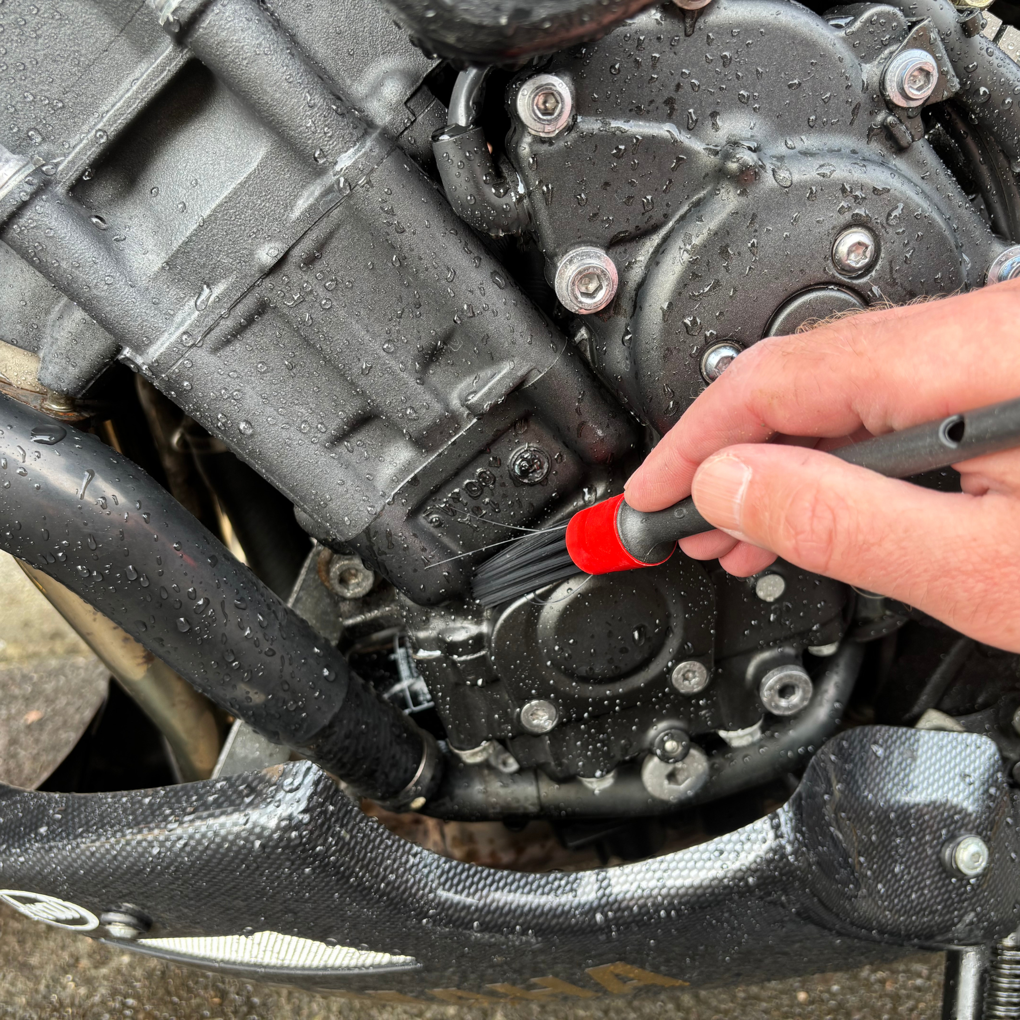 Person cleaning a motorcycle engine with a Ride It Rite detailing brush