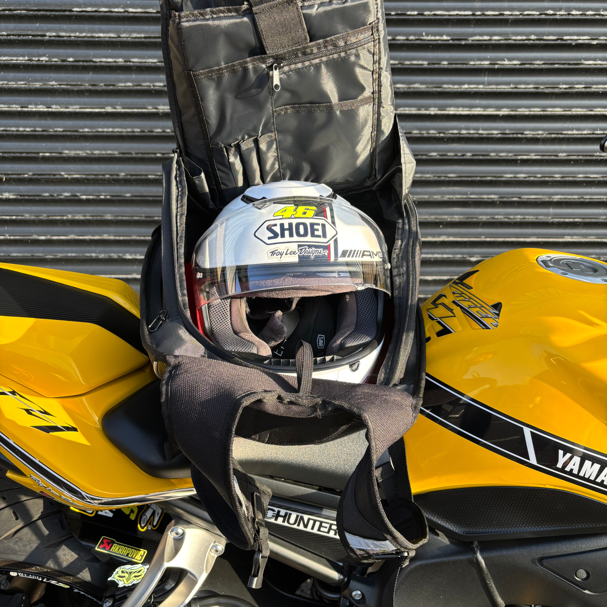 Helmet in a black Ride It Rite backpack on a yellow Yamaha motorcycle with a metallic background