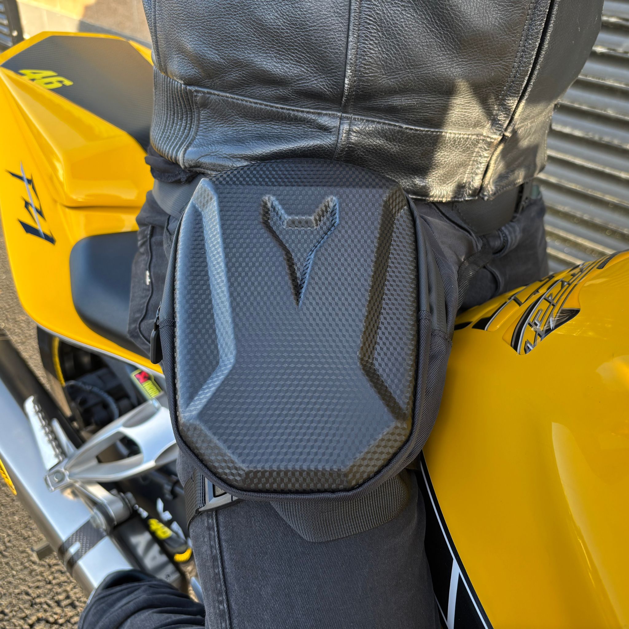 Close-up of a black Ride It Rite leg bag on a leg sitting on a yellow motorcycle.