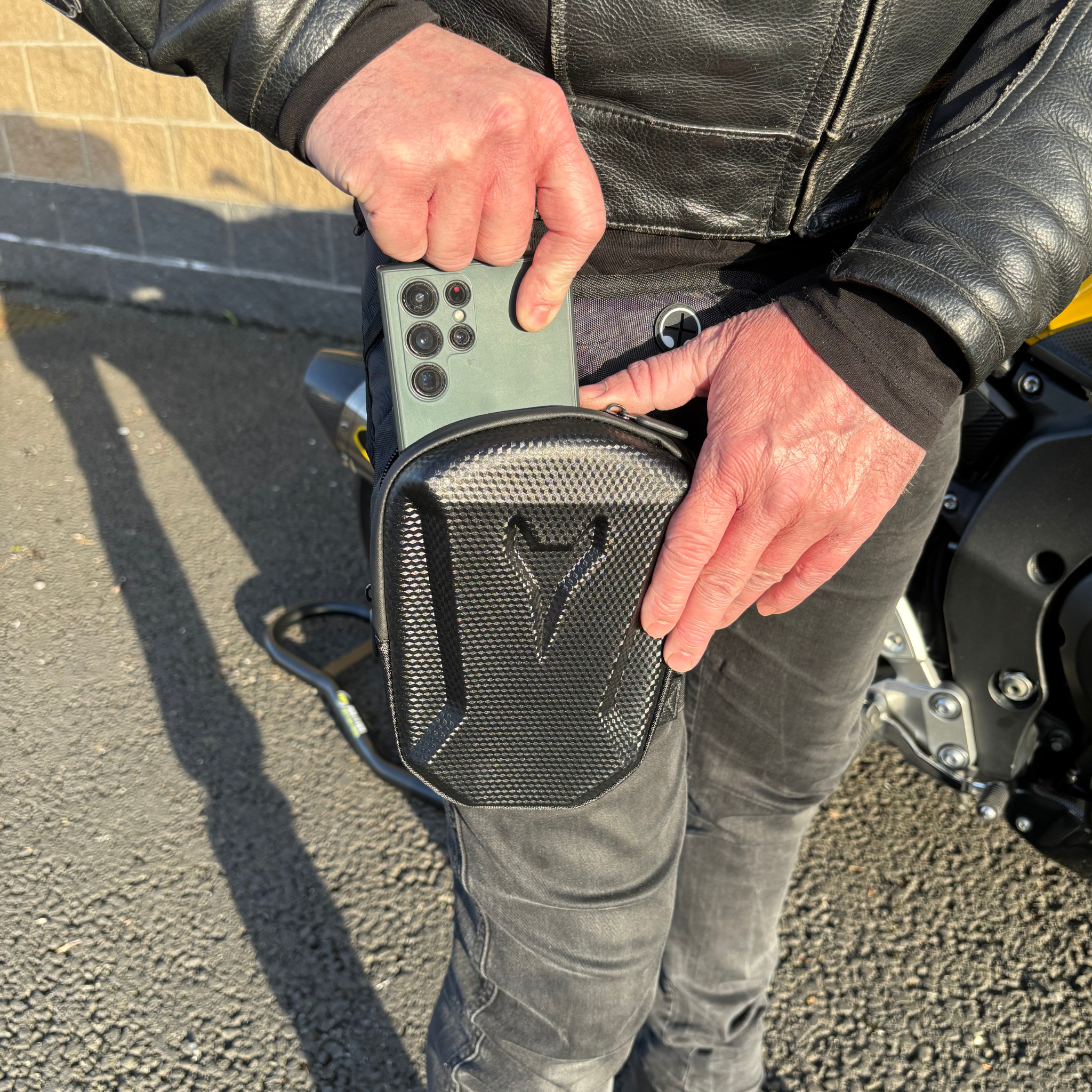 Person wearing a black Ride It Rite leg bag putting a mobile phone into it.