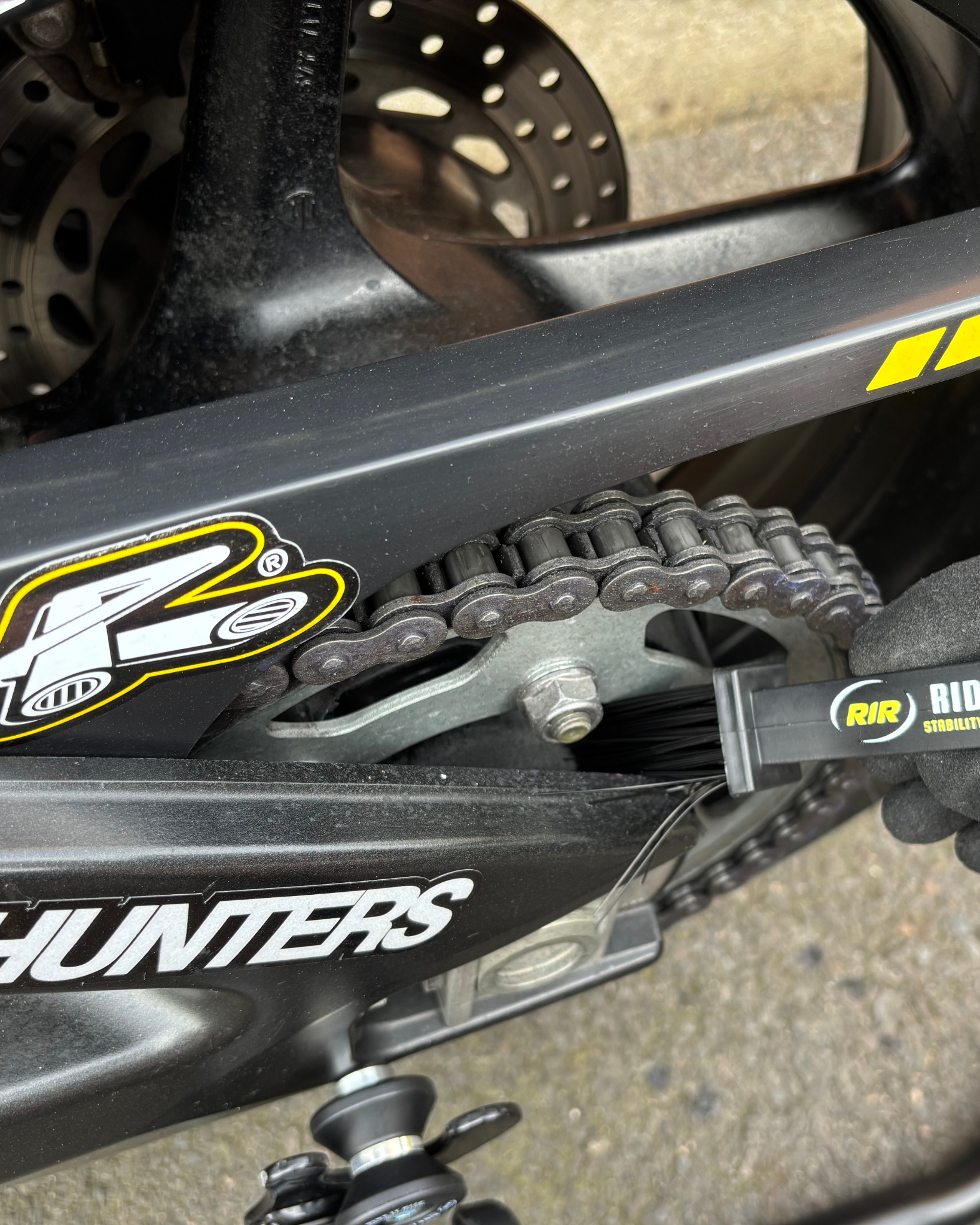 Close-up of a motorcycle chain and sprocket being cleaned with a Ride It Rite chain cleaning brush.