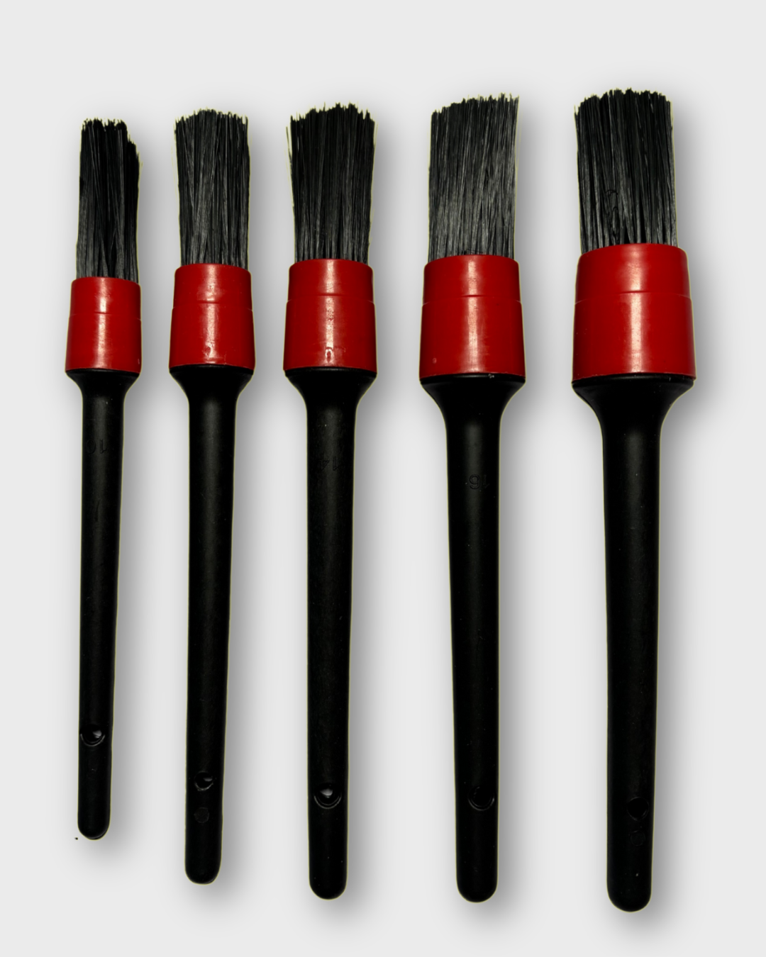 Five black-handled motorcycle detailing  brushes with red ferrules arranged in descending size order on a light gray background.