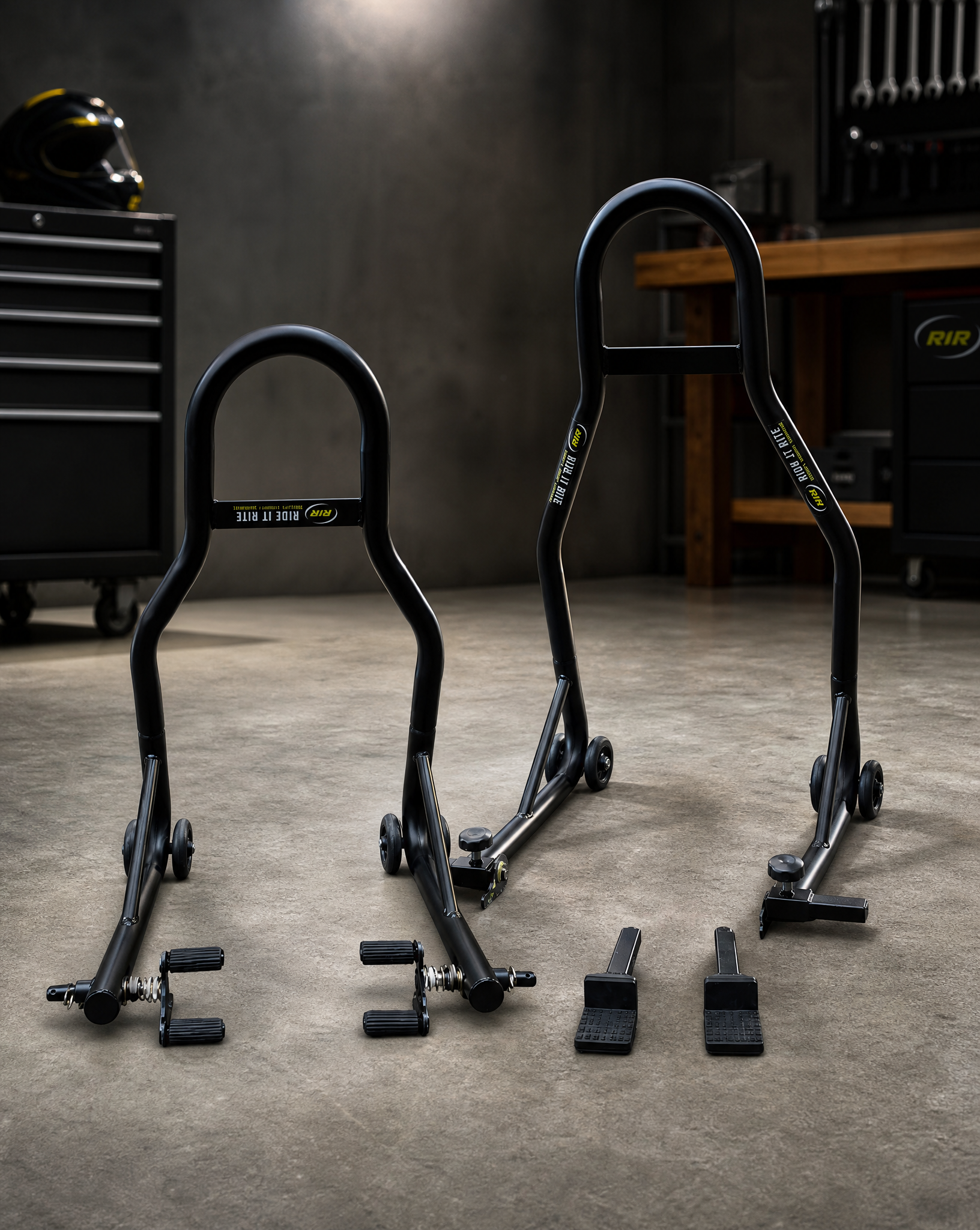 Set of black Ride It Rite motorcycle paddock stands on a concrete floor with tools and equipment in the background.