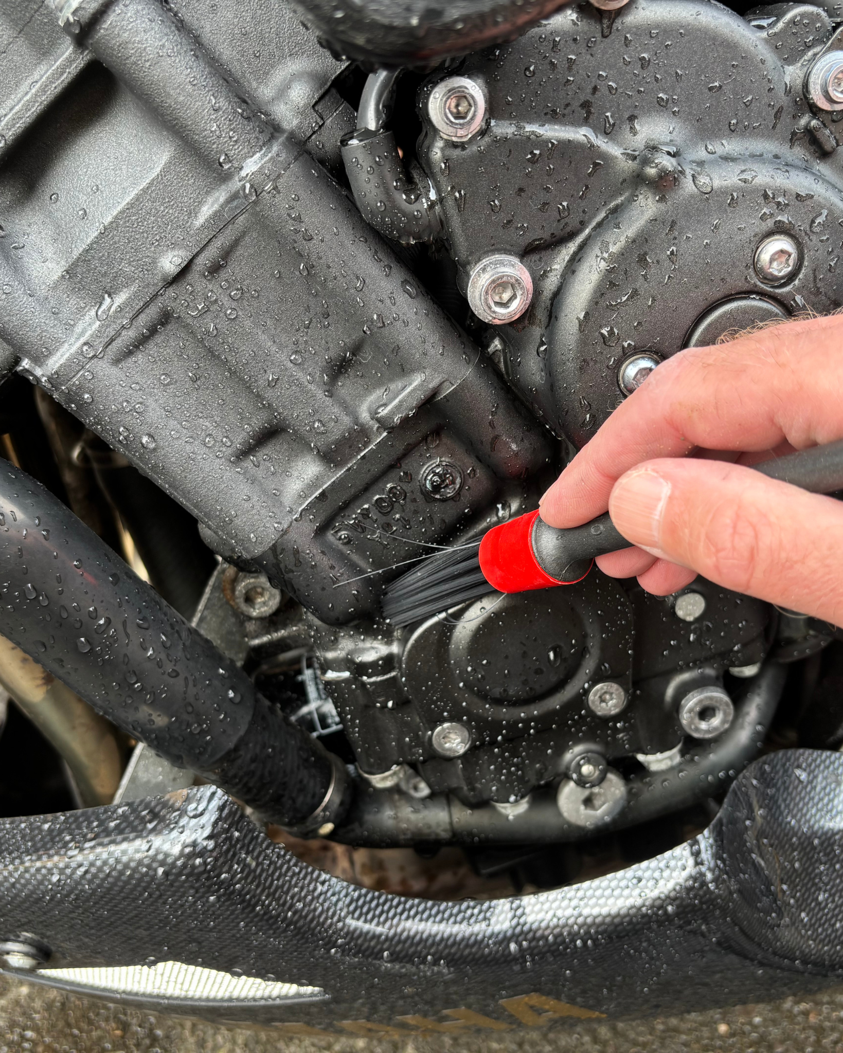 Person cleaning a motorcycle engine with a Ride It Rite detailing brush