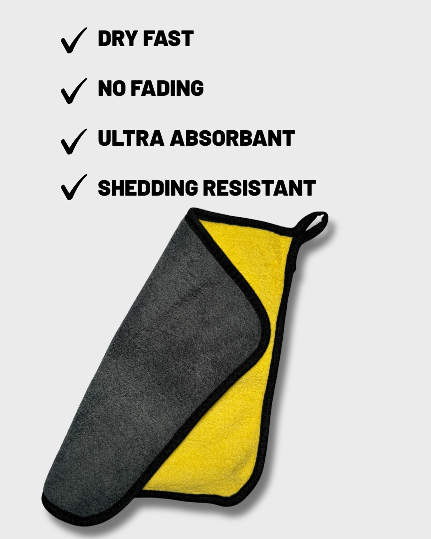 A two-sided microfiber cleaning cloth with a dark gray side and a bright yellow side, outlined in black. The cloth is shown on a light gray background with black text listing product features: 'DRY FAST', 'NO FADING', 'ULTRA ABSORBANT', and 'SHEDDING RESISTANT'.