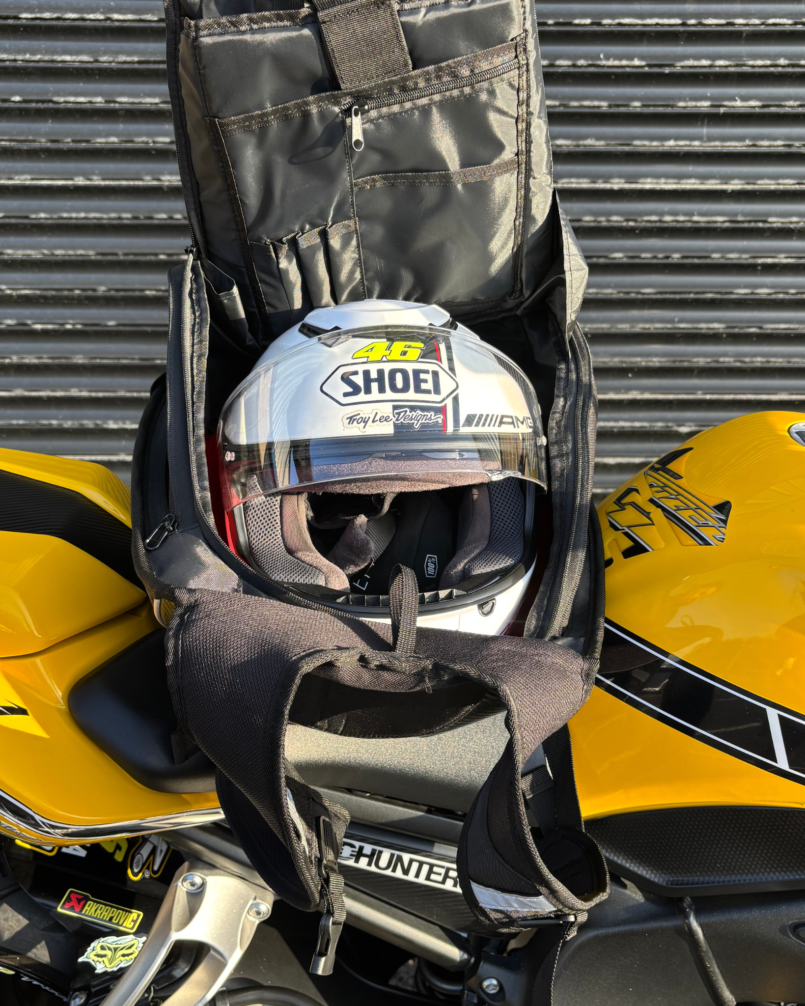 Helmet in a black Ride It Rite hard shell backpack on a yellow Yamaha motorcycle with a metallic background